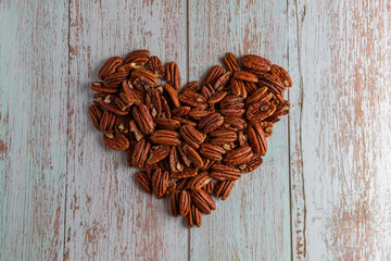 A heart made of natural pecan kernels on a wooden table, healthy fat and protein food, vegan,...