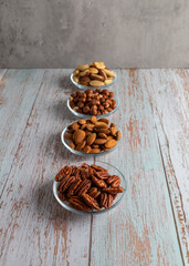 Four types of nuts in four glass bowls on a wooden table, healthy fat and protein food, vegan, ketogenic diet.