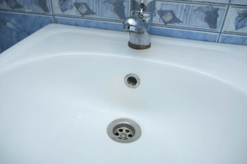 Water is dripping small drops from faucet in drain hole of the white sink in bathroom, closeup...