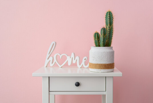 Home plant cactus cereus on bedside table near pink wall with word HOME