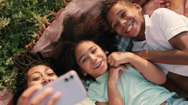 A happy afro-american family mother and her children are taking selfie photo while having picnic time outside at nature