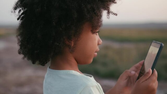 A pretty nice afro-american girl is taking photo of a sunset outside