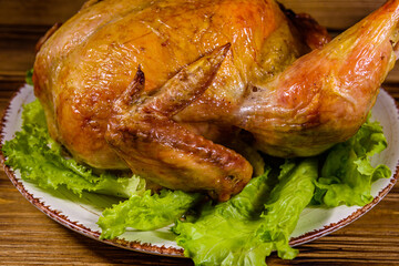 Plate with roasted whole chicken and lettuce leaves on a wooden table