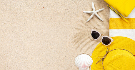 Fototapeta na wymiar Top view of sandy beach with stripy yellow and white towel frame, white sunglasses and sea shells. Background with copy space and visible sand texture. Summer concept