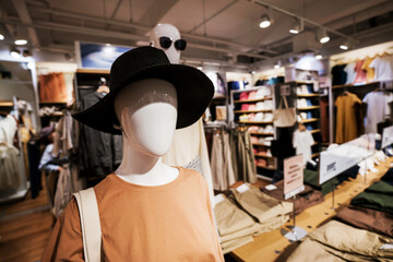Stylish female mannequin in big black hat standing in clothes retail store