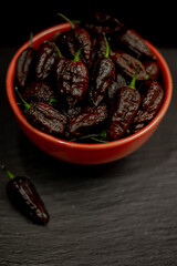 bowl of superhot peppers 7-pot madballz chocolate, habaneros, ghost peppers, extreme hot peppers on a black table