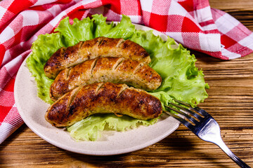 Plate with roasted sausages and lettuce leaves on a wooden table