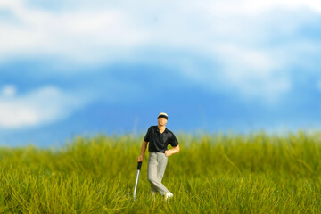Miniature people toy figure photography. A men golfer standing at meadow golf field on bright cloudy day morning.
