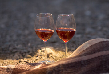 two glasses of red wine are standing on the seashore next to a blanket