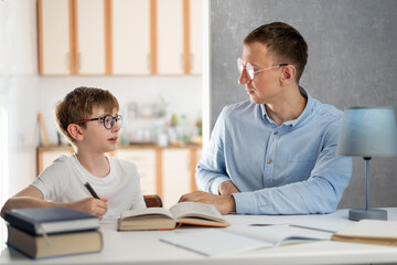Schoolboy teenager and young tutor study at home. Tutor helps the boy to do his homework. Home schooling