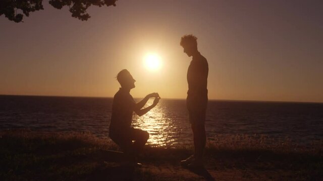 Silhouette of gay man kneeling to propose to boyfriend, romantic engagement