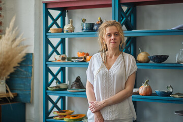 confident business owner posing in her office. in the background a wardrobe with ceramic dishes