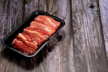 Raw beef meat in a black plastic container. Opened black plastic tray with raw cut meat