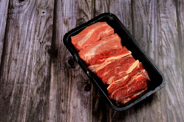Raw beef meat in a black plastic container. Opened black plastic tray with raw cut meat