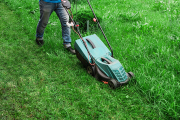 The gardener mows the lawn. Lawn mower on lush green grass in a modern garden.