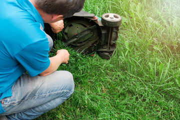 Broken lawn mower on lush green grass. The lawn mower is jammed with grass. A repairman repairs a lawn mower with tools.