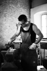 The blacksmith in the production process of metal products handmade in the forge. Blacksmith forging metal with a hammer. Black and white photo