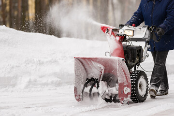 A man with a red snowplow cleans the lawn in front of the house from snow. Clearing the area from snowfall. - 450655326