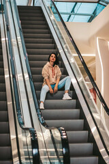 girl rides while sitting on the escalator. shopping mall, pretty brunette in a sporty style.