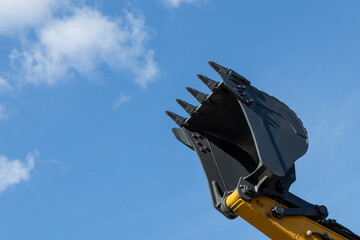 The lifted bucket of a new excavator against the background of the sky. Construction machinery...
