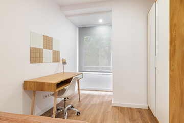 Minimalist room interior with modern comfortable workplace, wardrobe and window. Wooden table and floor with white wall and chair.