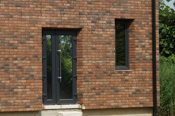 the wall of a private brown brick house with a black plastic glazed door and a window on the street
