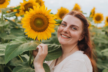 Happy Smiling female standing in sunflowers field on summer day. Harvest time. Summer vacation