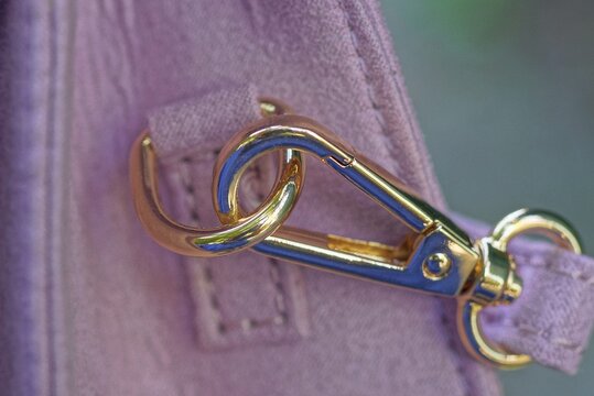 leather harness with a metal gold carabiner on the ring on a pink suede bag