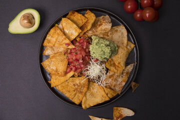Top view of nachos with guacamole sauce, chopped tomatoes and cheese on a black background