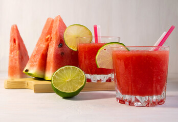 two glasses of watermelon cocktail, and slices of watermelon and lime on a white background