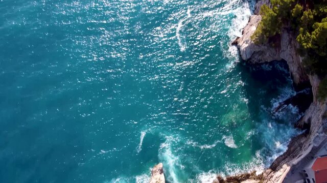 The drone hovered over the fortress on a rock and the camera slowly rises to meet the sun and waves from the sea.