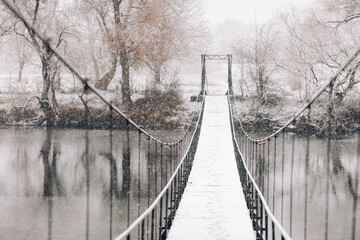 Pedestrian suspension bridge made of steel and wood across the river, winter