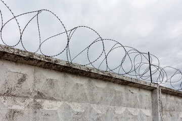 Concrete wall with barbed wire and gray sky