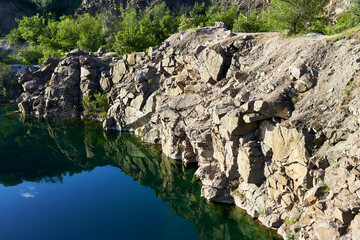 Fototapeta na wymiar Mountain lake in the summer. Panoramic view on old flooded granite quarry with radon water. Landscape with rock stones, green trees and clean pond