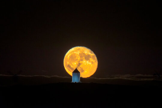 Old windmill in orange full moonrise with clouds, La Mancha, Consuegra, Spain.
