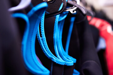 Closeup macro of wetsuits hung up on coat hangers in a wet room cloak room with shallow depth of...