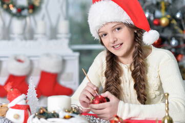 happy girl in Santa hat preparing for Christmas sitting at the table