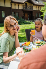 Smiling woman holding hand of blurred husband near cheerful kid with orange juice and food outdoors