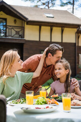 Man kissing smiling daughter near wife and food outdoors