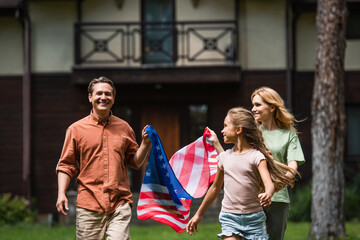 Obraz na płótnie Canvas Smiling man holding american flag near wife and daughter outdoors