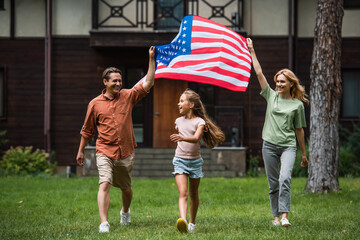 Happy kid walking on lawn near parents with american flag outdoors