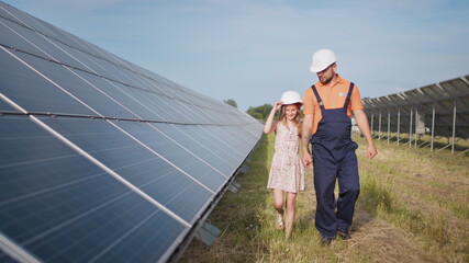 A father working in a solar power plant tells his daughter about his work, shows green energy, solar panels. Shooting at a solar power plant. The child studies solar energy