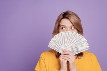 Photo of young pretty woman closing face bunch of dollars rich curious look empty space isolated over violet color background