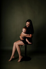 stylish mother in a black dress is sitting on a chair and playing with her baby daughter on a green isolated background with a place for text