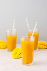 Freshly squeezed mango juice in glasses with a straw, ripe cut mango on a gray background