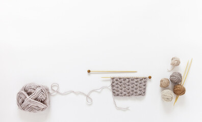 Delicate composition of knitting supplies in pastel beige colors on white background. Balls of wool and acrylic yarn, wooden knitting needles and the beginning of knitting warm fluffy scarf for autumn
