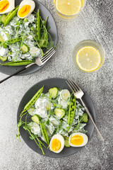 Salad with arugula, cucumbers and young peas with yogurt and boiled eggs with microgreens, lemon water in a glass, top view