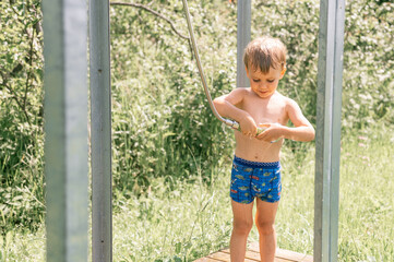 little four year old kid boy fun pours himself with cold water from a watering can from a outdoor...