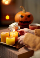 Fototapeta na wymiar holidays and leisure concept - woman's hand with match lighting candle at home on halloween