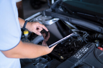 Auto mechanic with digital tablet at work making an engine repair diagnosis of a car in a mechanic garage